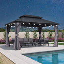 Grey hardtop gazebo with curtains and string lights, outdoor furniture by pool at night, patio shade solution.