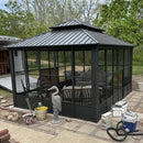 Gray sunroom hardtop gazebo with sliding doors, a perfect patio shade solution, outdoor furniture and mesh screen windows.