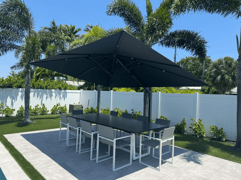 Large patio umbrella shading modern dining set amidst tropical greenery.