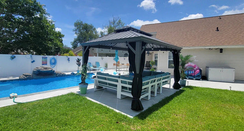 Black metal gazebo with curtains over a white outdoor dining set beside a swimming pool in a backyard