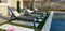 Four modern gray chaise lounges with cushions by a poolside, placed on artificial grass tiles