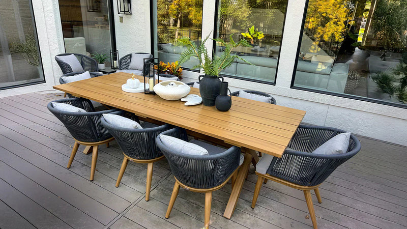 Long wooden outdoor dining table with black woven chairs on a modern patio