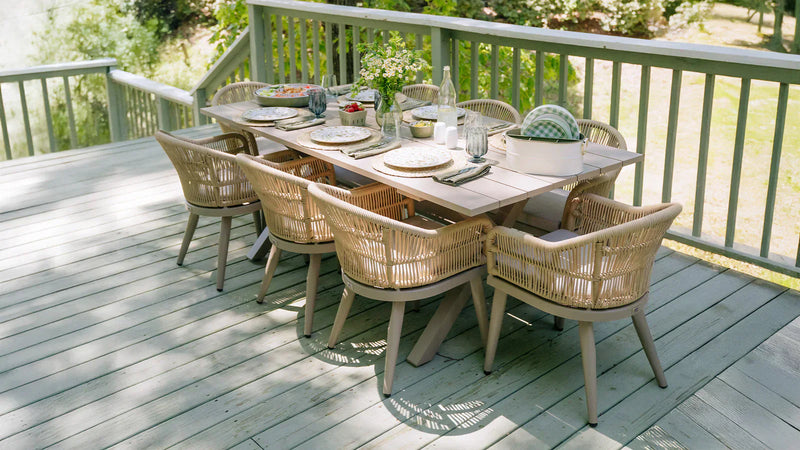Casual outdoor dining set on a light wooden deck, complete with a table, woven chairs, and natural surroundings