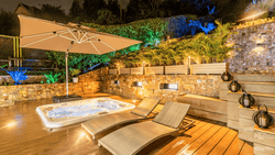 An outdoor patio at night with a hot tub, lounge chairs, and colorful lighting.