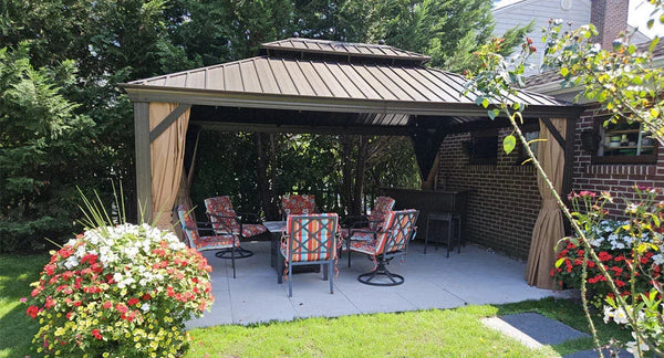 Black enclosed hardtop gazebo with metal roof and mesh screens, featuring indoor seating and positioned on a concrete patio in a residential backyard