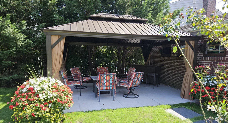 Black enclosed hardtop gazebo with metal roof and mesh screens, featuring indoor seating and positioned on a concrete patio in a residential backyard