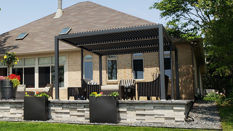 A sleek, modern pergola with a black slatted roof provides shade to a stylish outdoor living space. 