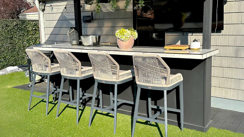 Outdoor bar counter with four woven rattan chairs and a black surface