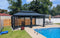 A black metal gazebo with mesh curtains set up beside a swimming pool in a backyard with a wooden fence.