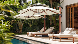 Two large, off-white patio umbrellas, mounted on a tall wooden pole, provide ample shade over a luxurious poolside lounging area.