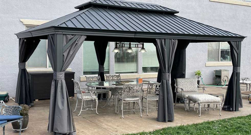 A spacious gazebo with a dark gray metal frame and roof stands on a concrete patio. 